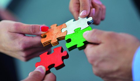 Vier Hände setzen vier große Puzzle-Teile zusammen